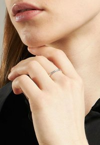 Närbild av en person som rör vid hakan med ena handen, iförd en delikat silverkedjeringsring på pekfingret.