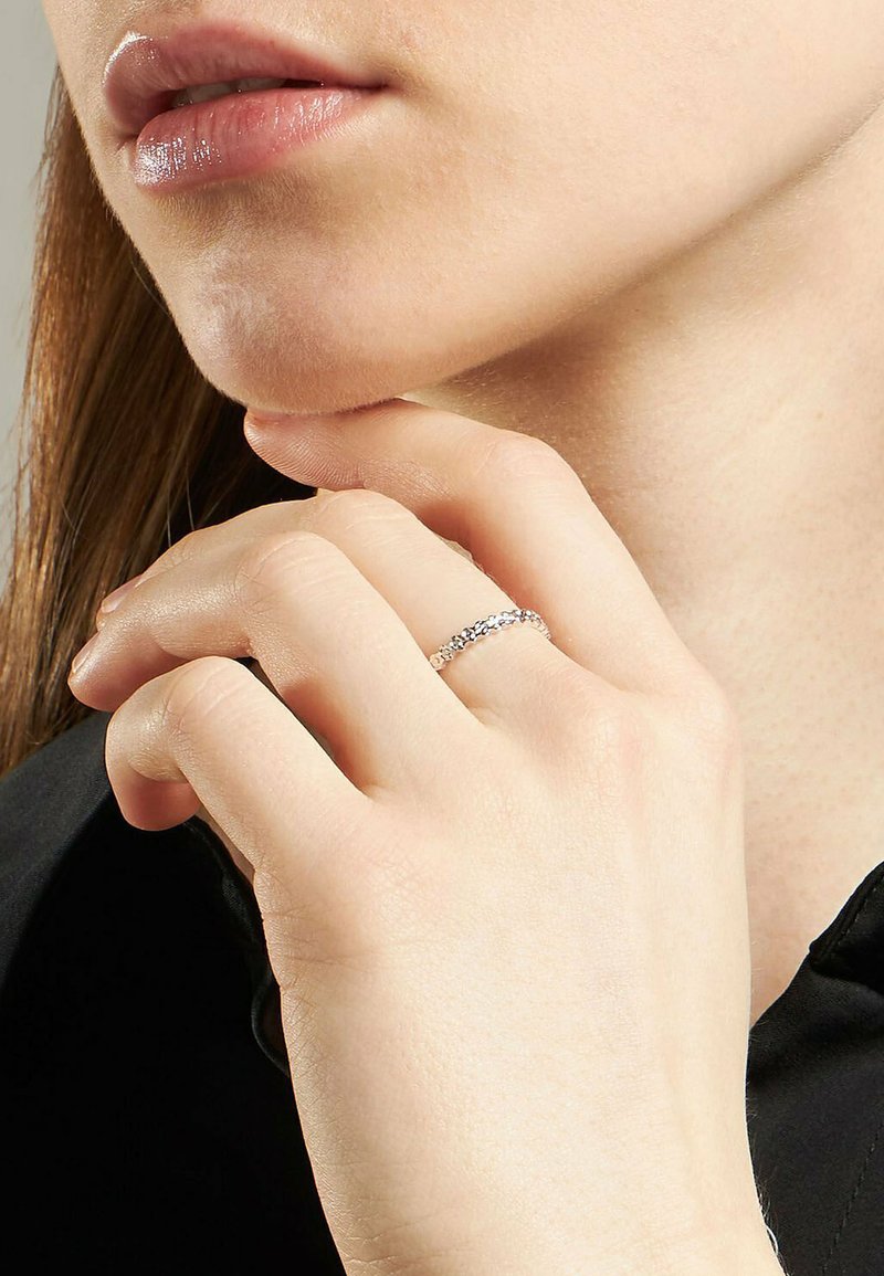 Närbild av en person som rör vid hakan med ena handen, iförd en delikat silverkedjeringsring på pekfingret.