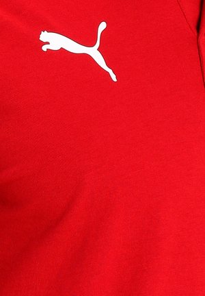 Rød stof t-shirt med et hvidt logo af en springende kat på venstre brystområde. Materialet ser glat ud med en tætsiddende design.