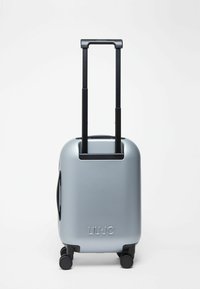 Valise rigide argentée avec poignée télescopique noire et quatre roues pivotantes noires, marquée "LIU·JO" sur la partie inférieure avant.
