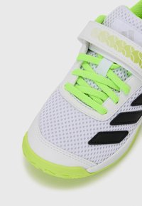 Scarpa sportiva bianca con parte superiore in rete, dettagli neri e lacci verde brillante. Presenta una cinghia con chiusura a strappo e suola con texture.