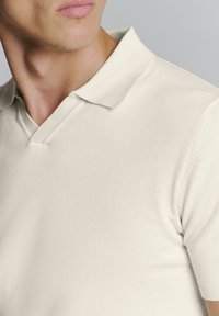 Beige polo shirt met korte mouwen, met een v-hals ontwerp, gebreide textuur en subtiele ribbelkraag.