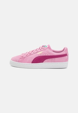 Niskie buty sportowe Puma z różowego zamszu z ciemniejszym różowym paskiem, białą gumową podeszwą i sznurowanym fasonem, widoczne z boku na białym tle.