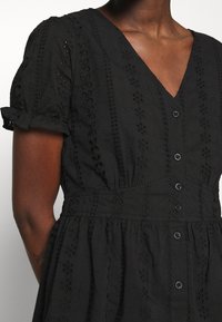 Svart bomullsklänning med v-ringning, korta volangärmar, knappstängning fram och dekorativ blommig broderi längs kroppen.