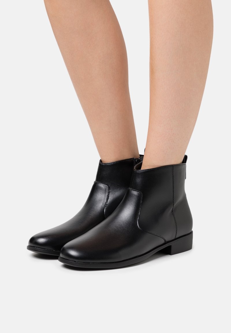 Mustat nahkakengät nilkkamittaisilla varrella, joissa on sileä pinta, matala korko ja elastiset sivupaneelit, jotka helpottavat jalkaan laittamista. Pistoletut yksityiskohdat saumoissa.