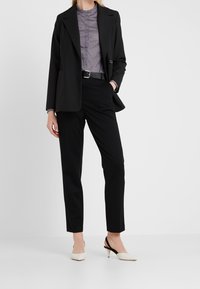 Blazer negro a medida sobre una camisa gris con cuello, pantalones negros y tacones beige con una correa negra. Diseño elegante con un ajuste estructurado.