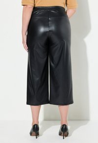 Culotte in finta pelle nera con design a gamba larga, dotati di un elastico in vita e di una superficie liscia e lucida. Tacchi visibili in basso.
