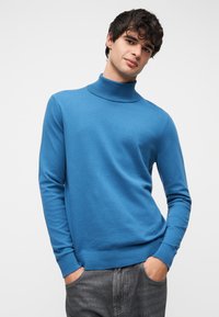 Μπλε πουλόβερ με ψηλό λαιμό και μακριά μανίκια, κατασκευασμένο από λείο πλεκτό ύφασμα, με ριμπ λαιμόκοψη και μανσέτες, συνδυασμένο με σκούρο γκρι τζιν.