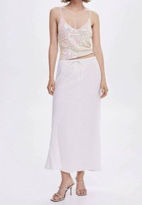 Camisole rose pâle ornée de paillettes avec des bretelles spaghetti, associée à une jupe maxi blanche à cordon de serrage et des sandales à talons hauts argentées.