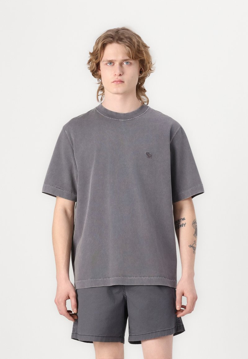 Šedé oversized bavlněné tričko s kulatým výstřihem a krátkými rukávy. Obsahuje jemnou výšivku loga na hrudi a viditelné švy.