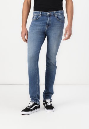 Dark blue denim jeans with a slim fit, five-pocket design, and slight fading, paired with black sneakers with white accents.