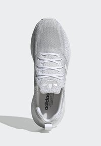 Fehér sportcipő, texturált kötött felsőrésszel, feltűnő fűzőkkel és párnázott talppal. A nyelvén logó található, és minimális díszítéssel rendelkezik.