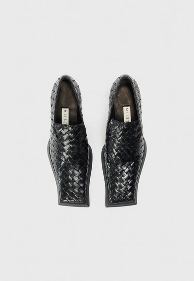 Scarpe slip-on in pelle intrecciata nera con suola piatta, caratterizzate da una superficie liscia e punta arrotondata. Design minimalista senza hardware visibile.