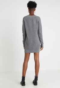 Robe-pull en maille grise à manches longues, texture côtelée, silhouette ajustée et col rond, associée à des bottines noires épaisses.