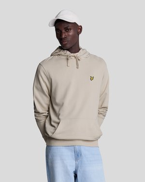 Felpa beige con cappuccio e coulisse, tasca a marsupio e piccolo logo giallo. Indossata con jeans azzurri chiari e un cappellino bianco. Texture liscia.
