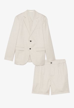 Blazer beige claro con dos botones negros y pantalones cortos de cintura elástica a juego, confeccionado en una tela texturada con un sutil patrón.