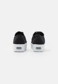 Schwarze Leinensneaker mit einer weißen Gummisohle, im Low-Top-Design und mit einem Logo-Tag an der Ferse. Schlichte Steppnähte.