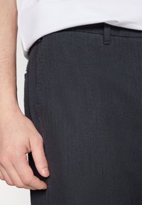 Tmavě šedé kalhoty s herringbone vzorem a rovným střihem. Mají pas s opaskem, boční kapsu a čisté švy.