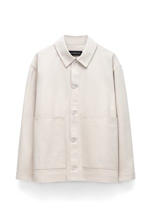 Beige langärmelige Hemdjacke mit Kragen und zwei großen Fronttaschen, dargestellt vor einem weißen Hintergrund.