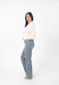 Maglione bianco a maglia, cropped, abbinato a jeans dritti a vita alta di un blu chiaro. Sandali trasparenti completano l'outfit.