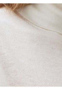 Zbliżenie na jasnobeżową dzianinę oraz fragment swetra z żebrowanym golfem.