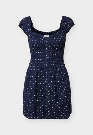 Marineblauw kort jurkje met witte polkadots, knoopsluiting aan de voorkant, gerimpelde taille en gerimpelde mouwtjes.