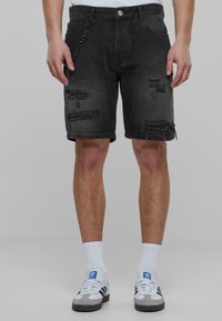 Shorts de mezclilla negra con patrones desgastados, un acento de cadena plateada y un ajuste relajado, que terminan justo por encima de la rodilla.