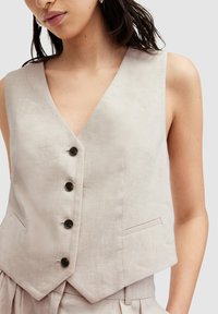 Ljusbeige linneväst med djup V-ringning, fem svarta knappar och sidofickor. Texturerad yta med en skräddarsydd passform.