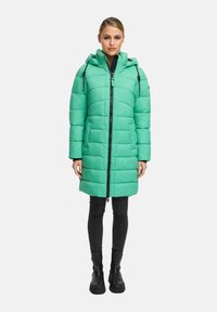 Long, padded coat in bright mint green. Features a zip front, adjustable hood, and black accents. Worn over black skinny jeans and boots.