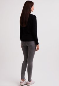 Svart tröja med långa ärmar, parat med grå tight jeans. Vita sneakers med rosa detaljer. Släta texturer och figurnära design.