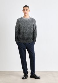 Maglione grigio e nero lavorato a maglia con un motivo testurizzato, abbinato a pantaloni blu scuro e scarpe in pelle nere. Design semplice e dalla vestibilità rilassata.