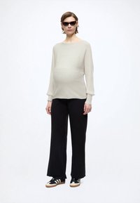 Svetlobéžový rebrovaný dlhý rukáv top v kombinácii s čiernymi širokými nohavicami a čiernymi teniskami s bielymi a béžovými prvkami; modelka je tehotná.