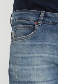 Jeans in denim, lavaggio azzurro chiaro, con design a cinque tasche, leggero sfilacciamento sui bordi delle tasche e dettagli di cucitura a contrasto.
