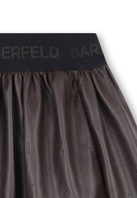 Bruine leren rok met een geplooid ontwerp, voorzien van een zwarte tailleband met het "KARL" logo. De gestructureerde oppervlakte heeft subtiele reliëfletters.