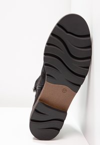 Semelle de botte noire avec motif ondulé, semelle intermédiaire marron et indication de la taille 37, présentée sur fond blanc.