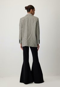Sacou cu un design geometric alb-negru, asortat cu pantaloni flared negri mulați, evidențiind un material neted și o croială ajustată.