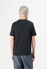 Black short-sleeve t-shirt with a straight cut, round neckline, soft texture, and no visible patterns or logos, viewed from the back.
