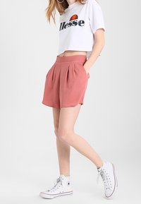 Bílý krátký tričko s logem "ellesse", růžové plisované šortky a bílé vysoké tenisky. Hladká látka a volný střih.