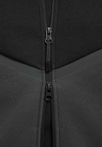 Chaqueta negra con cremallera y un panel texturizado gris. Presenta cremalleras dobles en el centro y un acabado de tela suave, que enfatiza un diseño moderno.