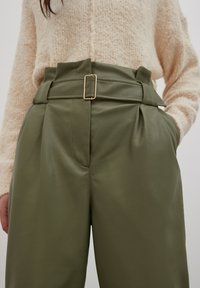 Olijfgroene high-waisted broeken van nepleer, met een brede riem en een rechthoekige gouden gesp, en een geplooid ontwerp aan de voorkant.