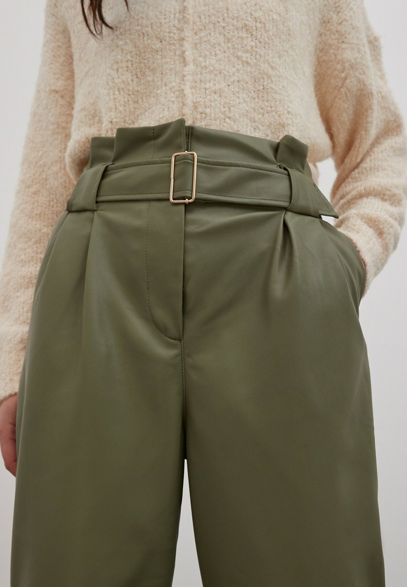 Olijfgroene high-waisted broeken van nepleer, met een brede riem en een rechthoekige gouden gesp, en een geplooid ontwerp aan de voorkant.