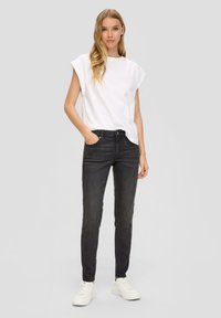 Witte shirt met korte mouwen, zwarte slim-fit jeans en witte sneakers. De outfit heeft een eenvoudig lijnenspel en een casual stijl.