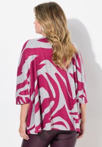 Top grigio oversize con motivo zebra magenta, vestibilità larga e maniche a tre quarti. Abbinato a leggings viola lucidi.