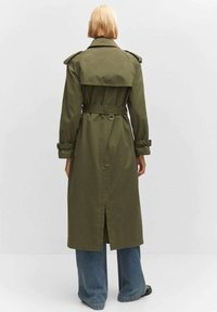 Trencz oliwkowo zielony z paskiem w talii, pagonami na ramionach i rozcięciem z tyłu. Wykonany z wytrzymałej tkaniny, charakteryzuje się klasycznym fasonem.