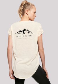 Light beige t-shirt with short rolled sleeves, featuring a mountain graphic and text "LOST IN NATURE" on the back. Soft texture.