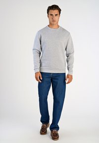 Felpa grigia in cotone con colletto tondo, polsini e vita a costine, abbinata a jeans di denim blu e scarpe marroni.