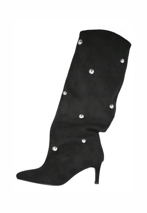 Bota de ante negra hasta la rodilla con punta afilada, tacón de aguja delgado y tachuelas decorativas plateadas. Textura suave con un acabado blando.