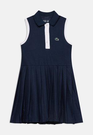 Robe polo sans manches bleu marine avec patte de boutonnage blanche, jupe plissée et petit logo crocodile vert sur la poitrine.