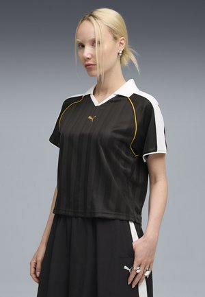 Schwarz gestreiftes Trikot mit einem weißen Kragen und gelben Akzenten. Verfügt über ein Logo auf der Brust und einen entspannten Schnitt, kombiniert mit schwarzen Hosen.