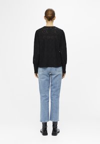 Pull en maille noir texturé, à coupe large et manches ballons, associé à un jean droit bleu clair et des bottines noires.
